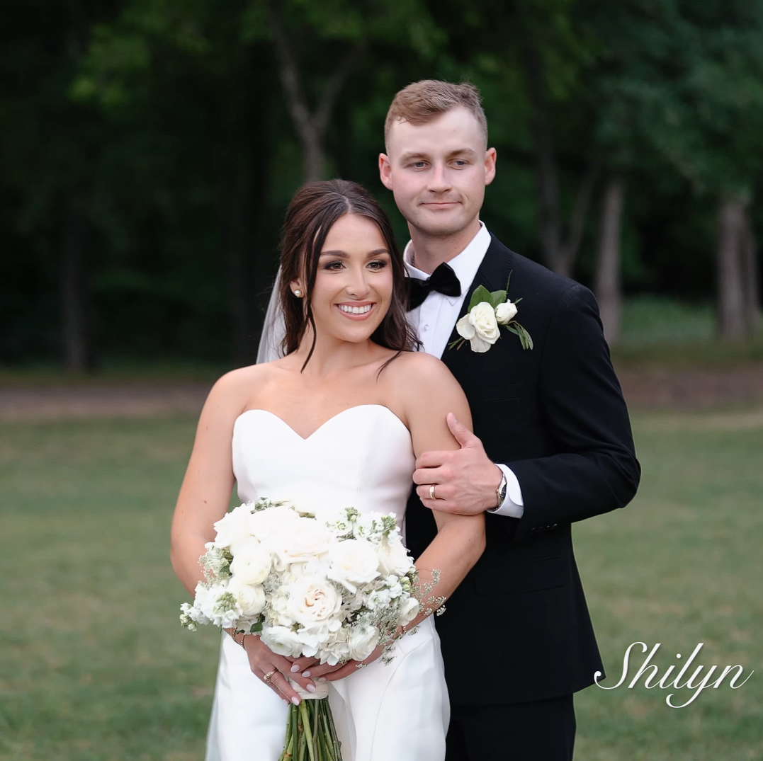 Couple in wedding attire standing outdoors with a blurred green background