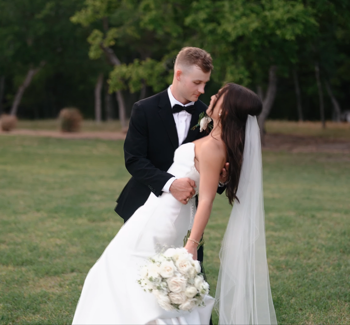 Man in a tuxedo and woman in a wedding dress holding each other outdoors.